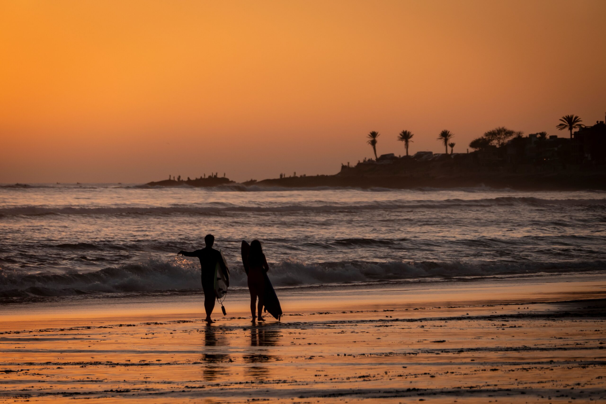 Surfer walking the beach at sunset, one of the best surf spots in Morocco